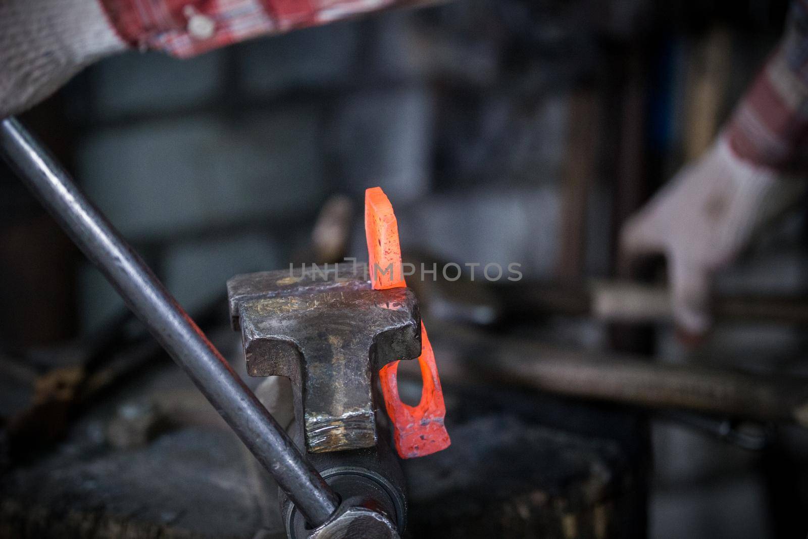 Workspace of blacksmith. Blacksmith working with red hot metal workpiece of new hammer in the vise. Telephoto shot