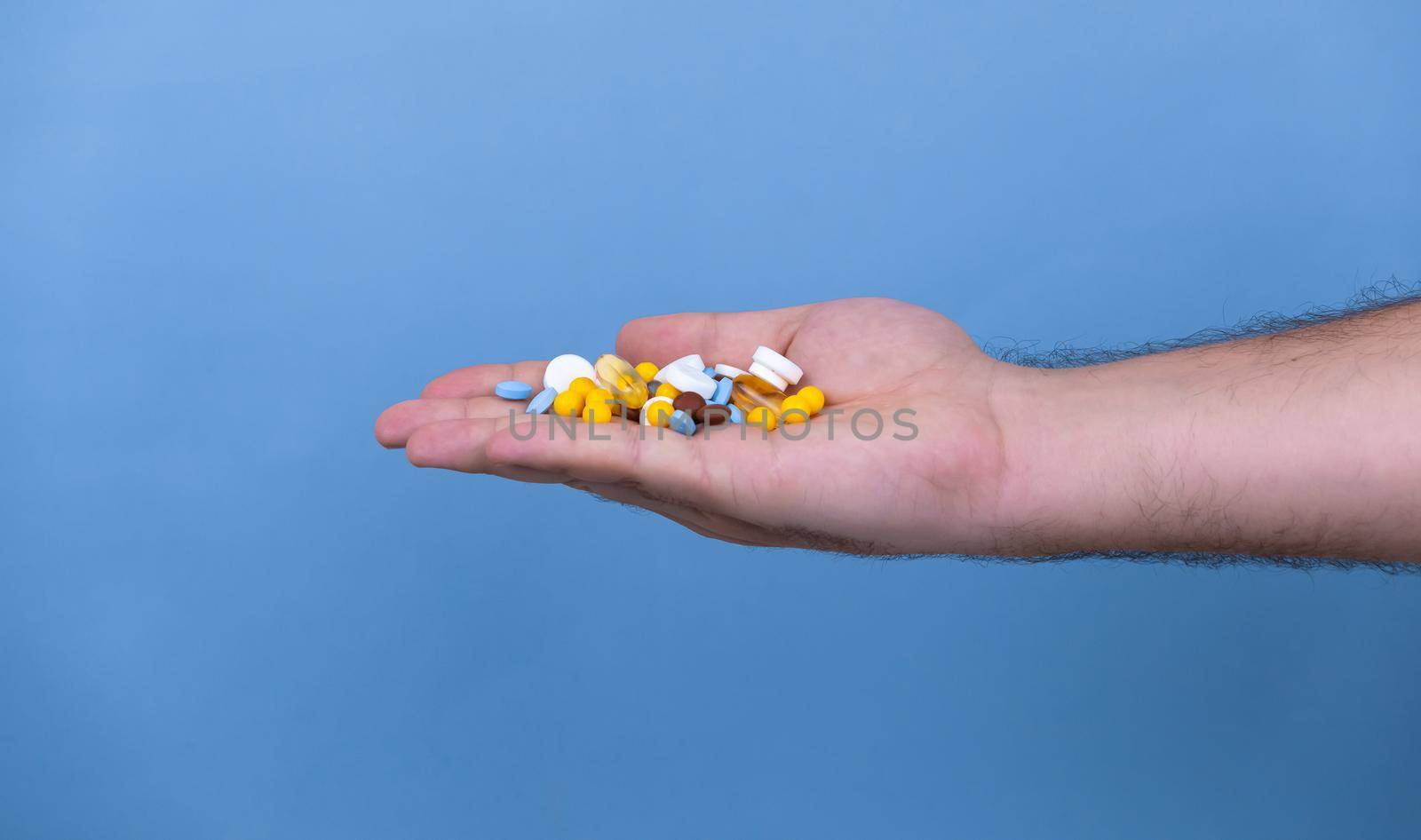 A pile of multi-colored pills in a male hand. A man holds pills in his hand. The concept of medicine, illness, health.
