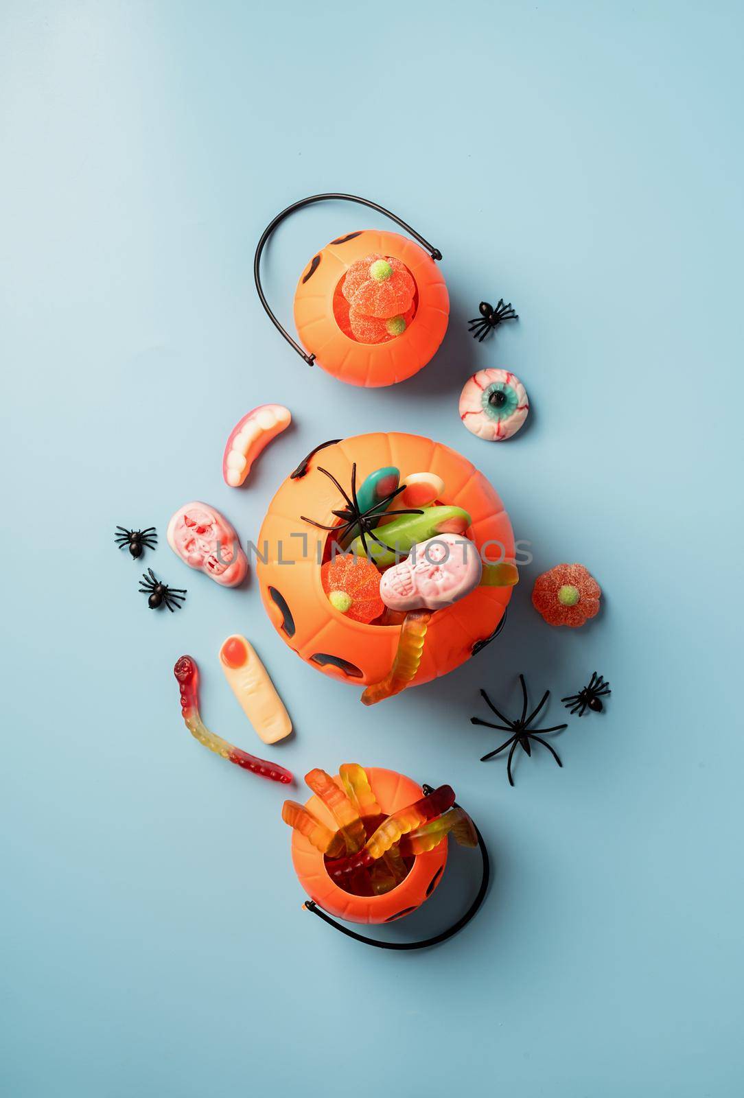 Halloween concept. Various halloween sweets in a pumpkin pot top view on blue solid background. Halloween party greeting card mock up
