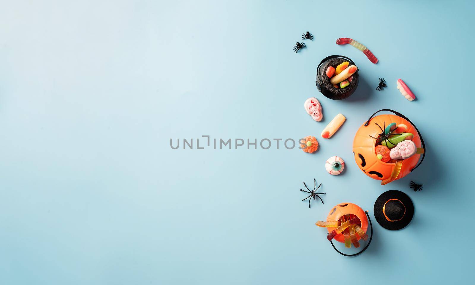 Various halloween sweets and candies in a pumpkin pot top view on blue solid background with copy space by Desperada