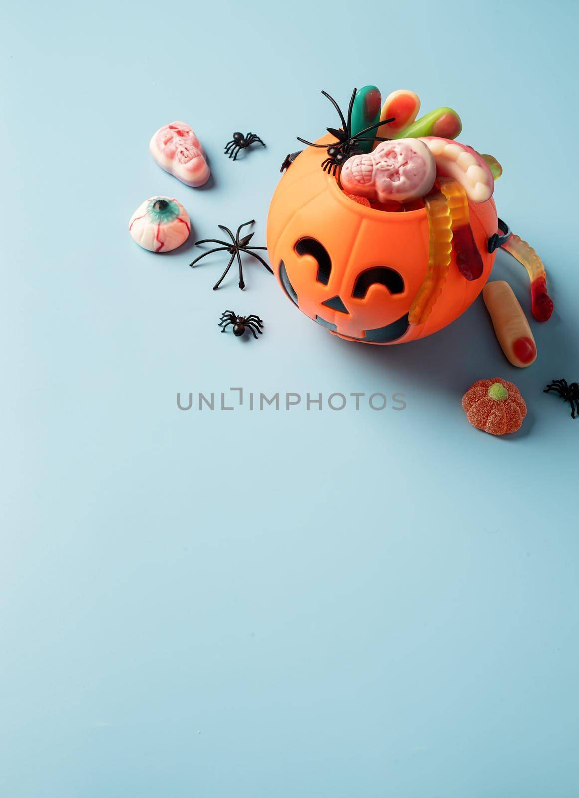 Various halloween sweets and candies in a pumpkin pot top view on blue solid background with copy space by Desperada