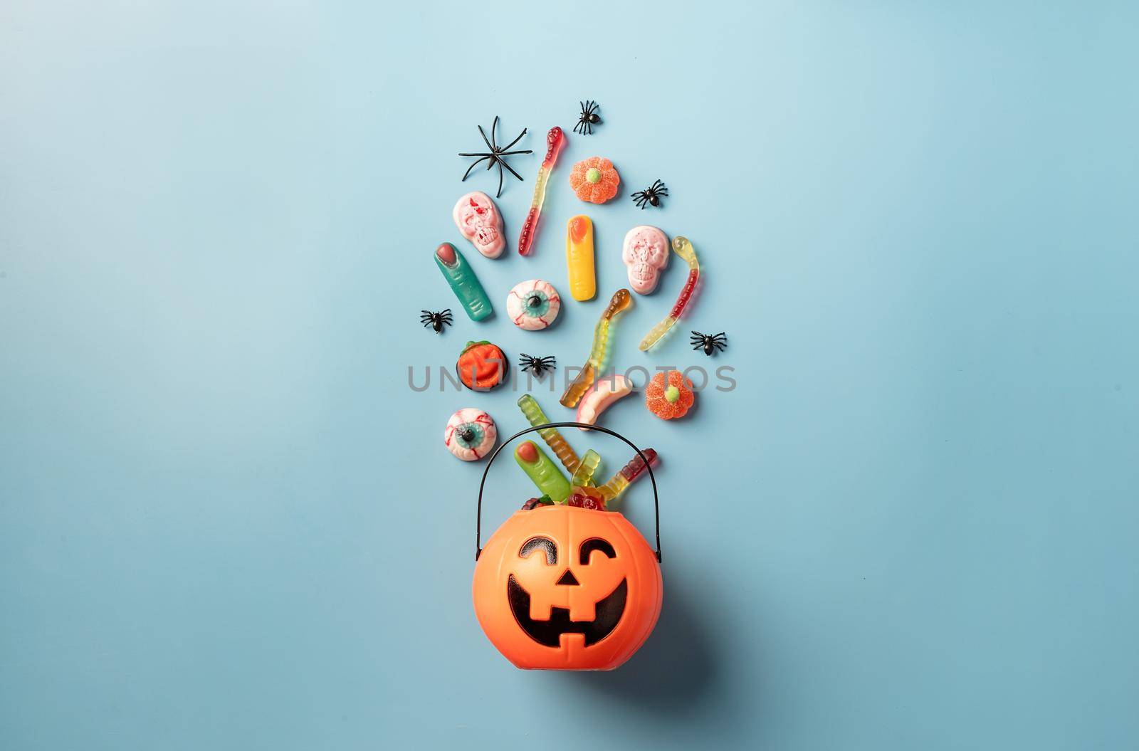 Various halloween sweets and candies in a pumpkin pot top view on blue solid background by Desperada