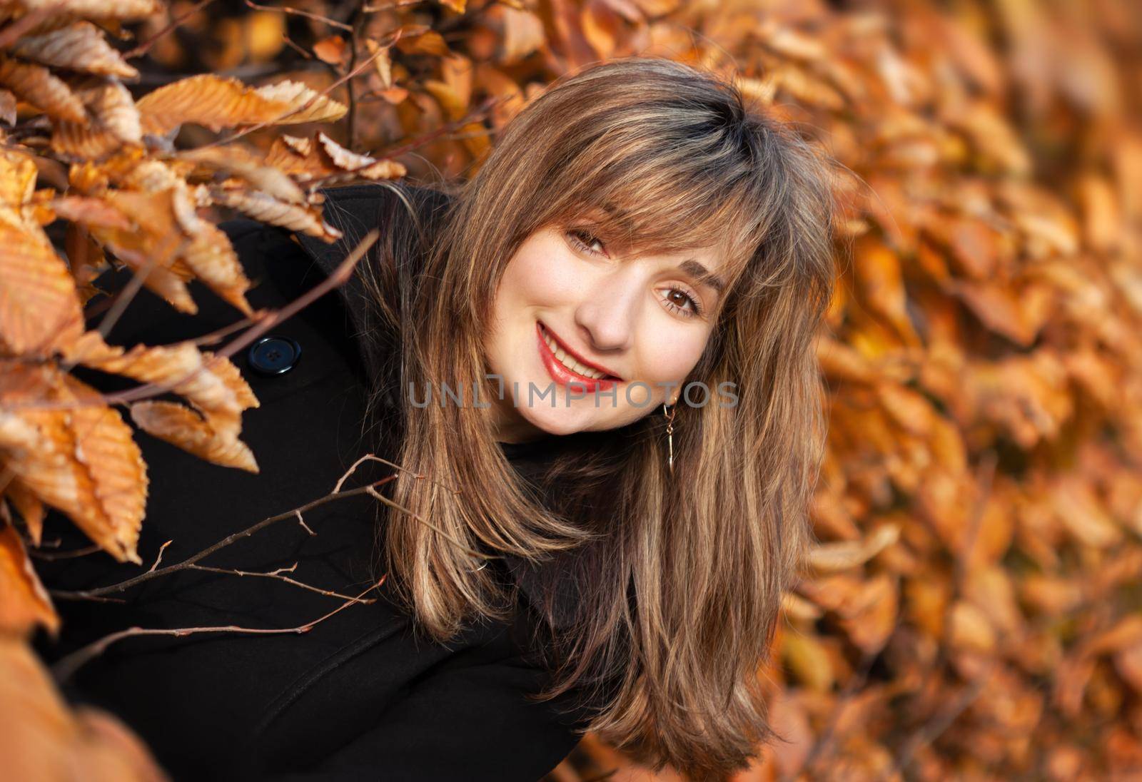 Smiling happy girl portrait with autumn leaves. Young woman among golden autumn leaves. Romantic moment in warm light. Park with yellow leaves and autumn atmosphere.