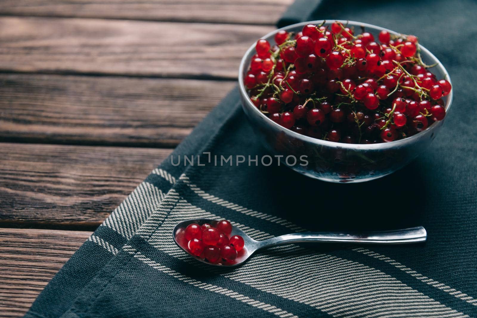 Fresh red currant in a bowl and spoon on rustic wooden background.