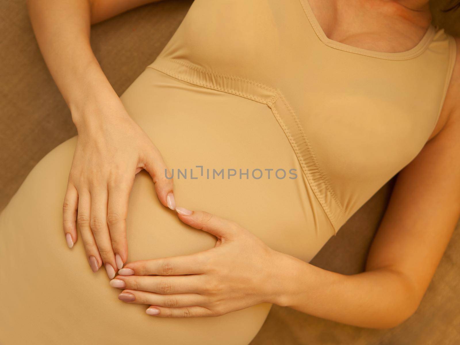 pregnant belly. woman hands in heart shape. Pregnant woman holding heart shaped hands on her belly. Mothernity brown colors