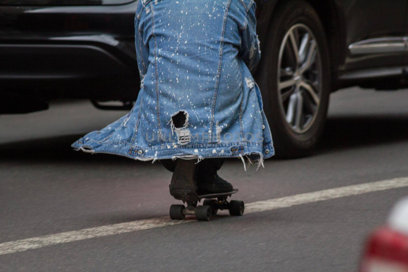 Man rides a skateboard sitting on a dividing strip on a city street, TELEPHOTO SHOT