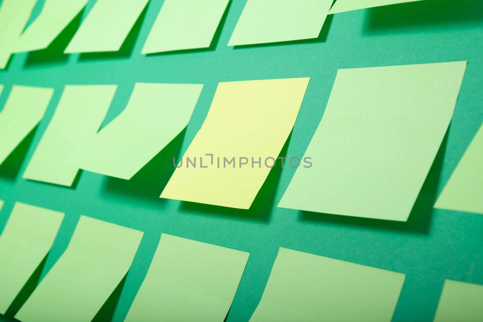 one yellow sticker and many light green sticky notes on a green background, selective focus by natashko