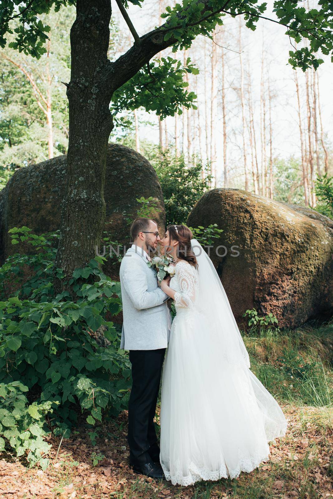 Bride and groom on wedding day, hugging, standing near a rock or a large stone by lunarts