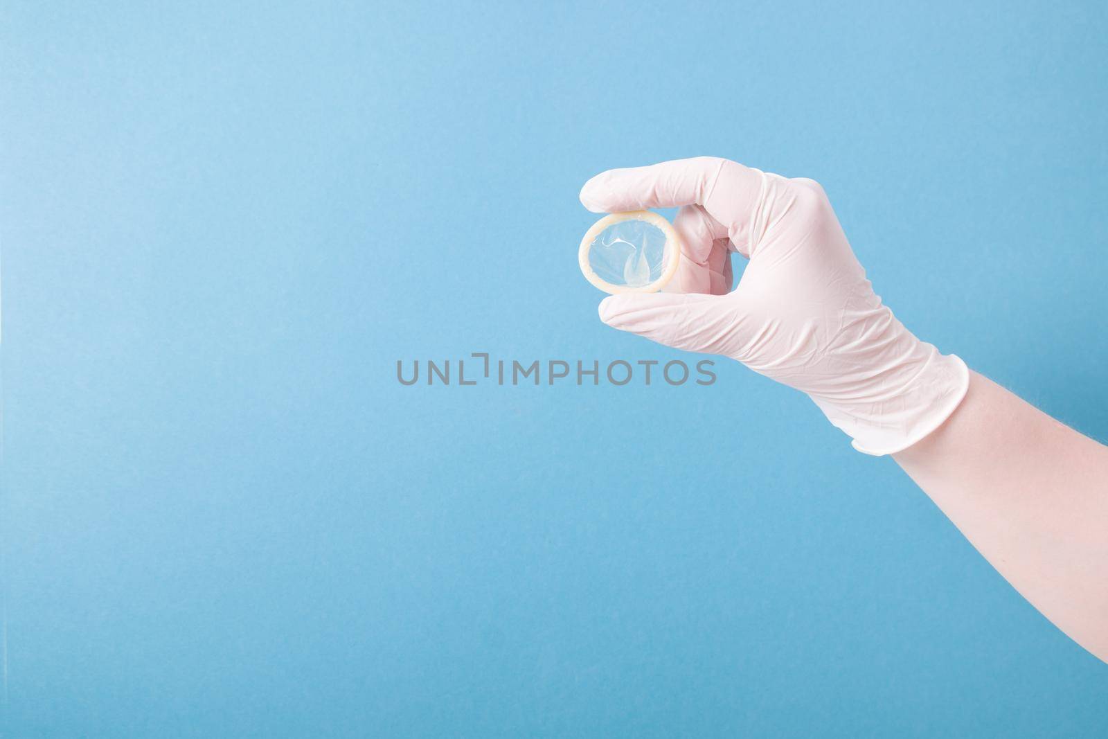 hand in a white medical rubber glove holds a condom without packaging on a blue background, copy space by natashko