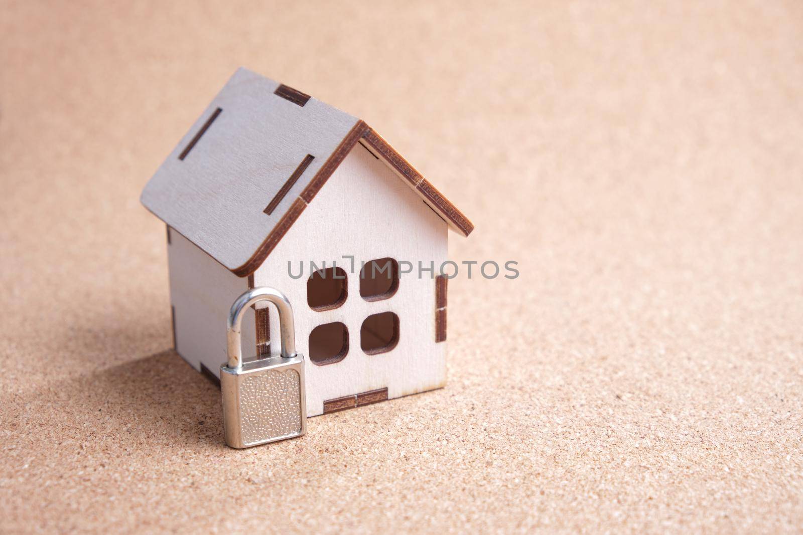 wooden toy house and a small padlock on a cork board, property protection concept by natashko