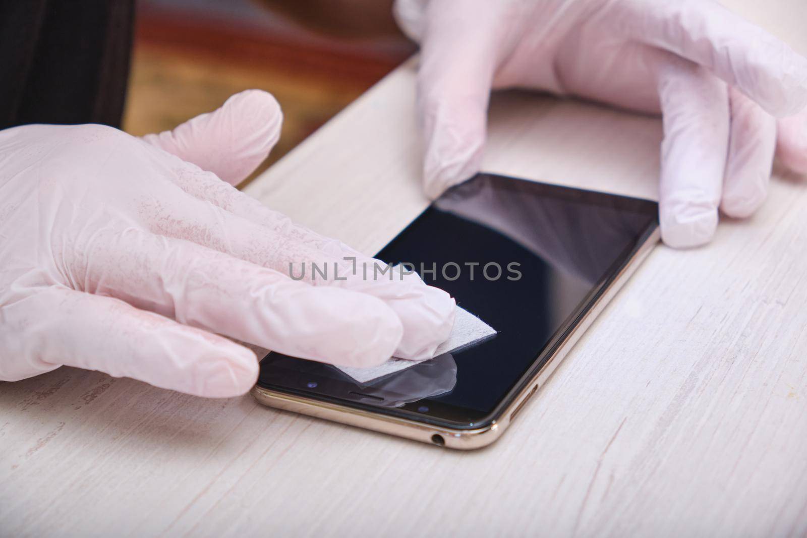 a man in rubber gloves wipes the glass of his smartphone with a damp cloth before gluing on the protective glass by natashko