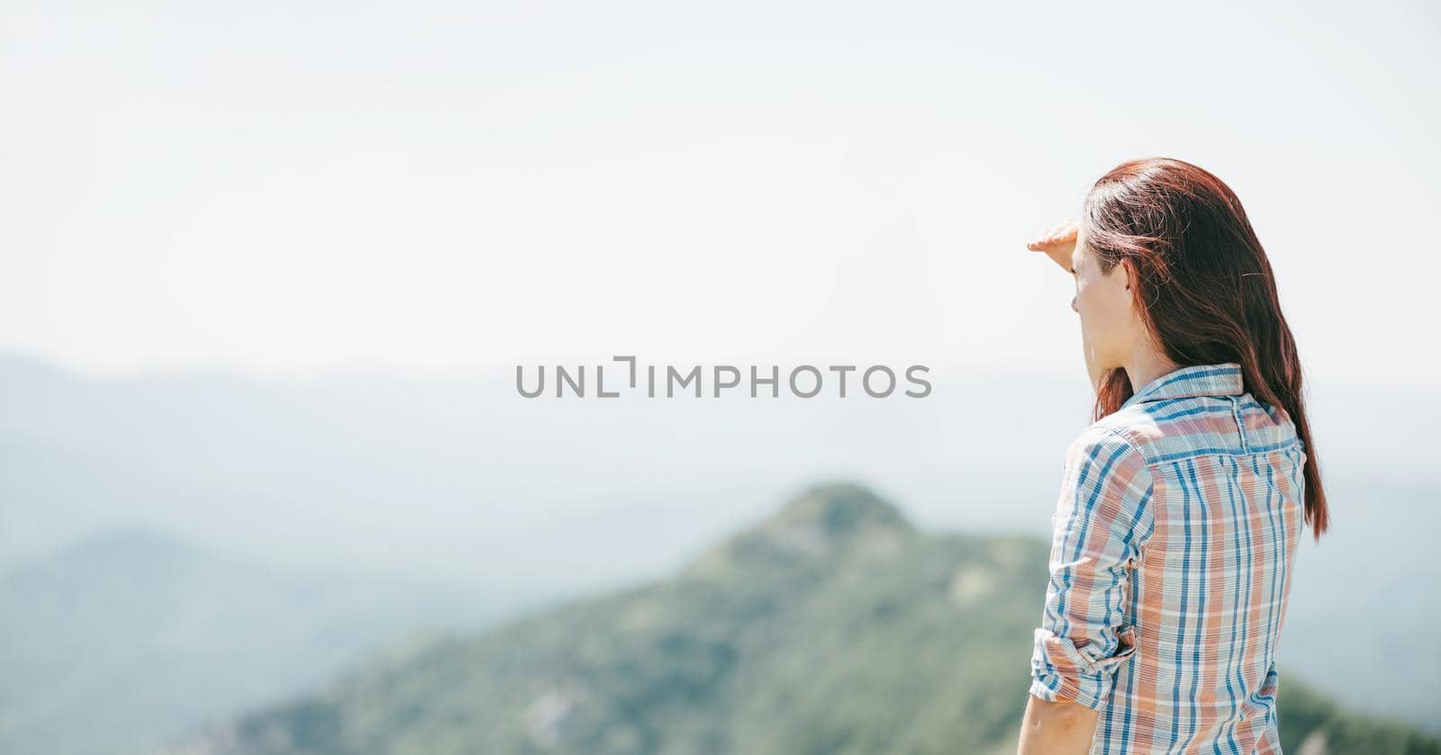 Young woman standing high in mountains and looking into the distance in summer outdoor.