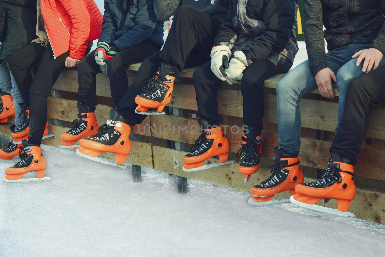 Teenagers in orange skate on the ice.