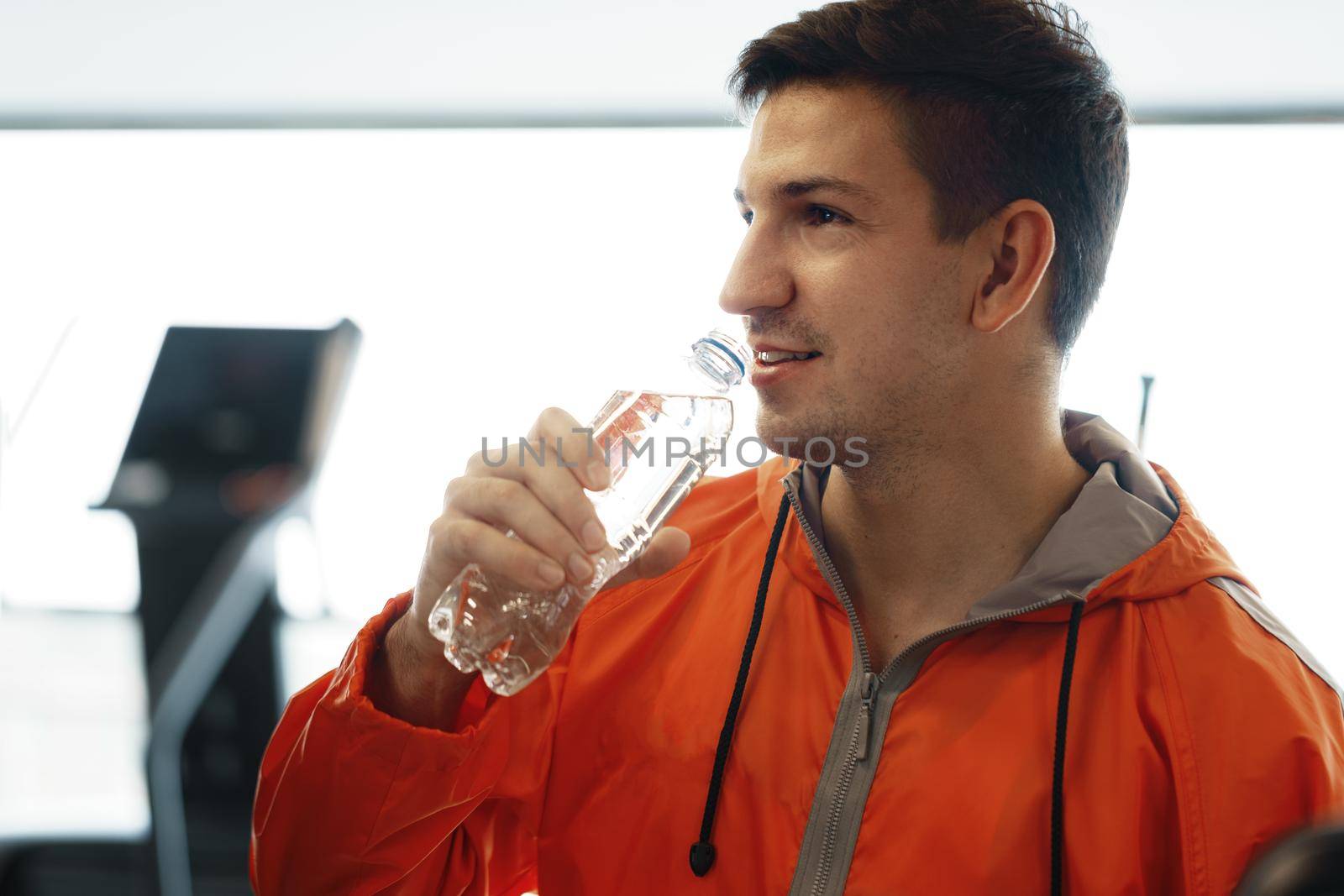 Portrait of young man drinking some water from a bottle in a gym, close up