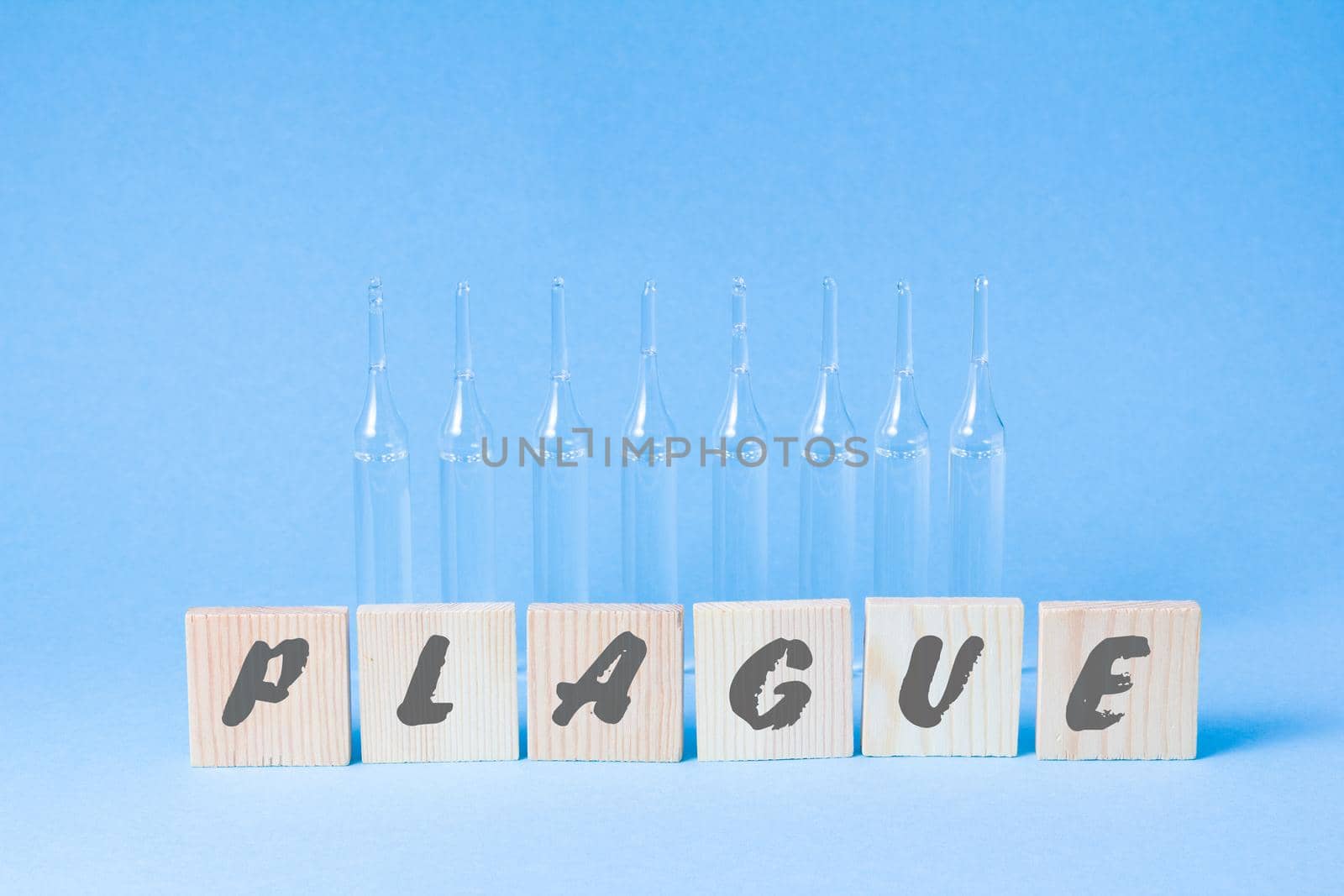 several glass ampoules standing in a row and wooden squares with the inscription plague, plague 2020 concept, blue background, copy space
