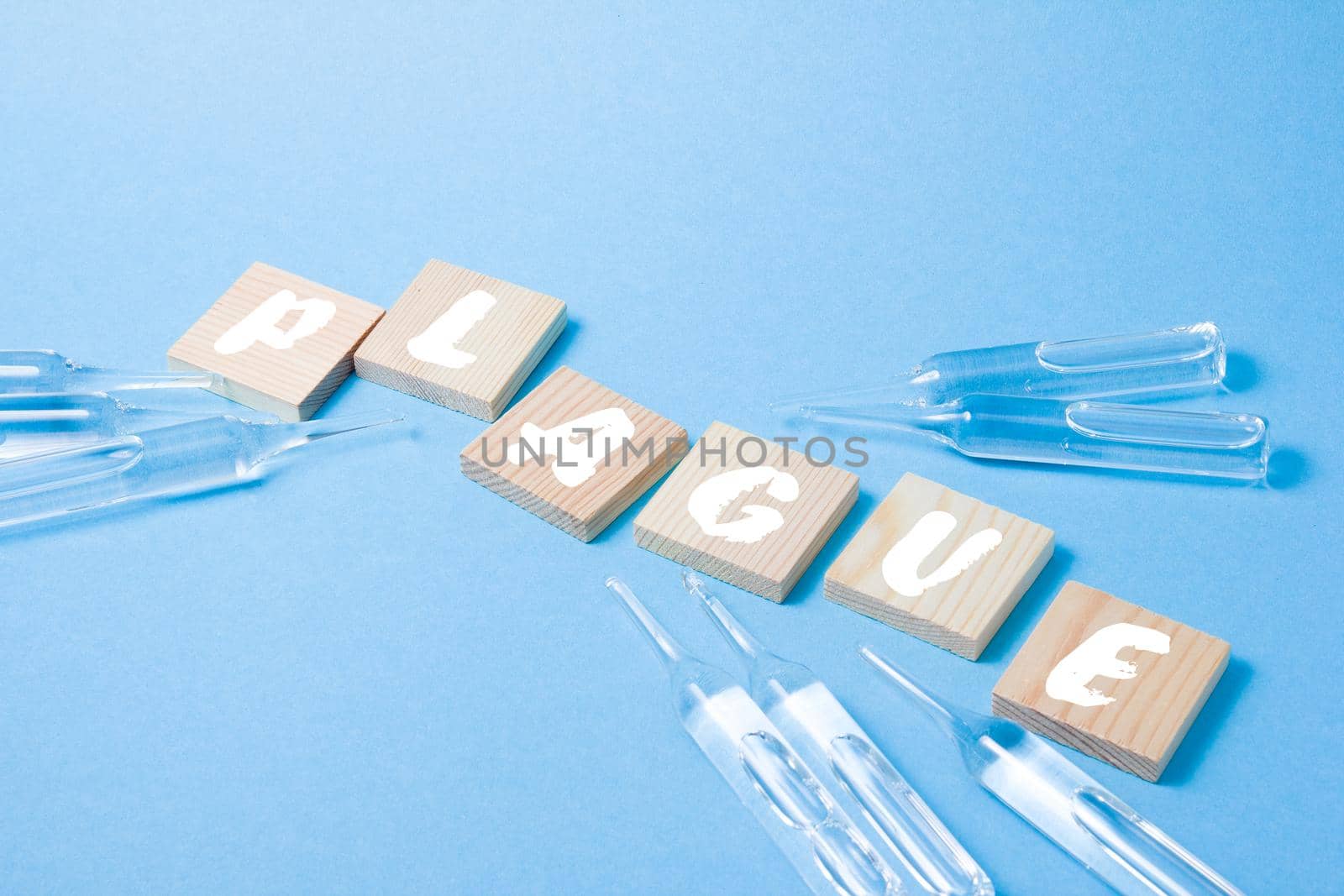several glass ampoules and wooden squares with the inscription plague, plague 2020 concept, blue background, copy space, top view