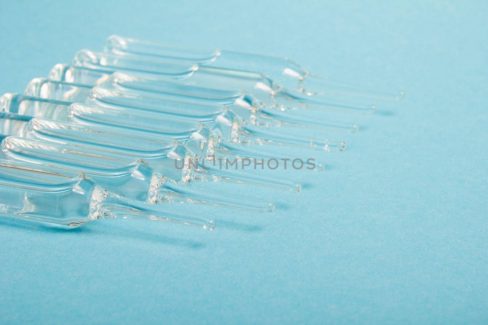 several large glass ampoule with drugs on a blue background copy space
