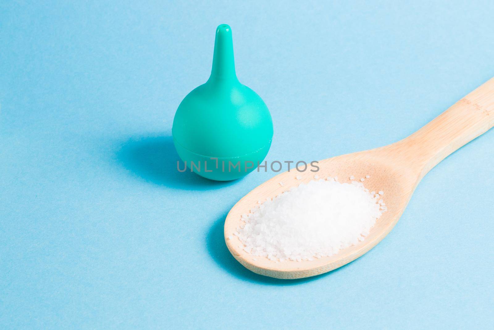 enema for the nose and a wooden spoon with sea salt on a light blue background, copy space, washing the nose with salt water using an aspirator by natashko