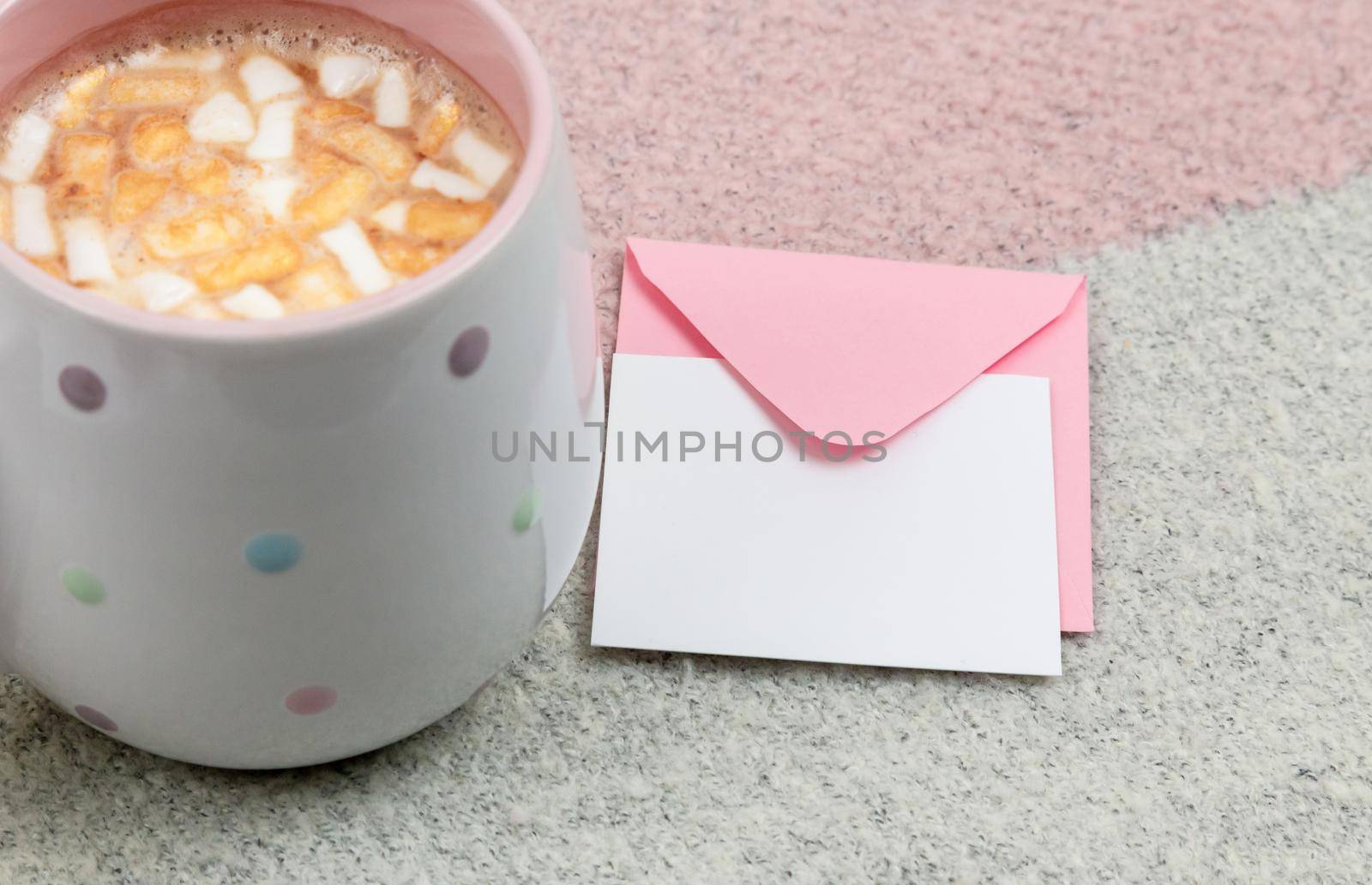 marshmallow cocoa mug and an envelope with a letter on a on pink and beige background. Top view.