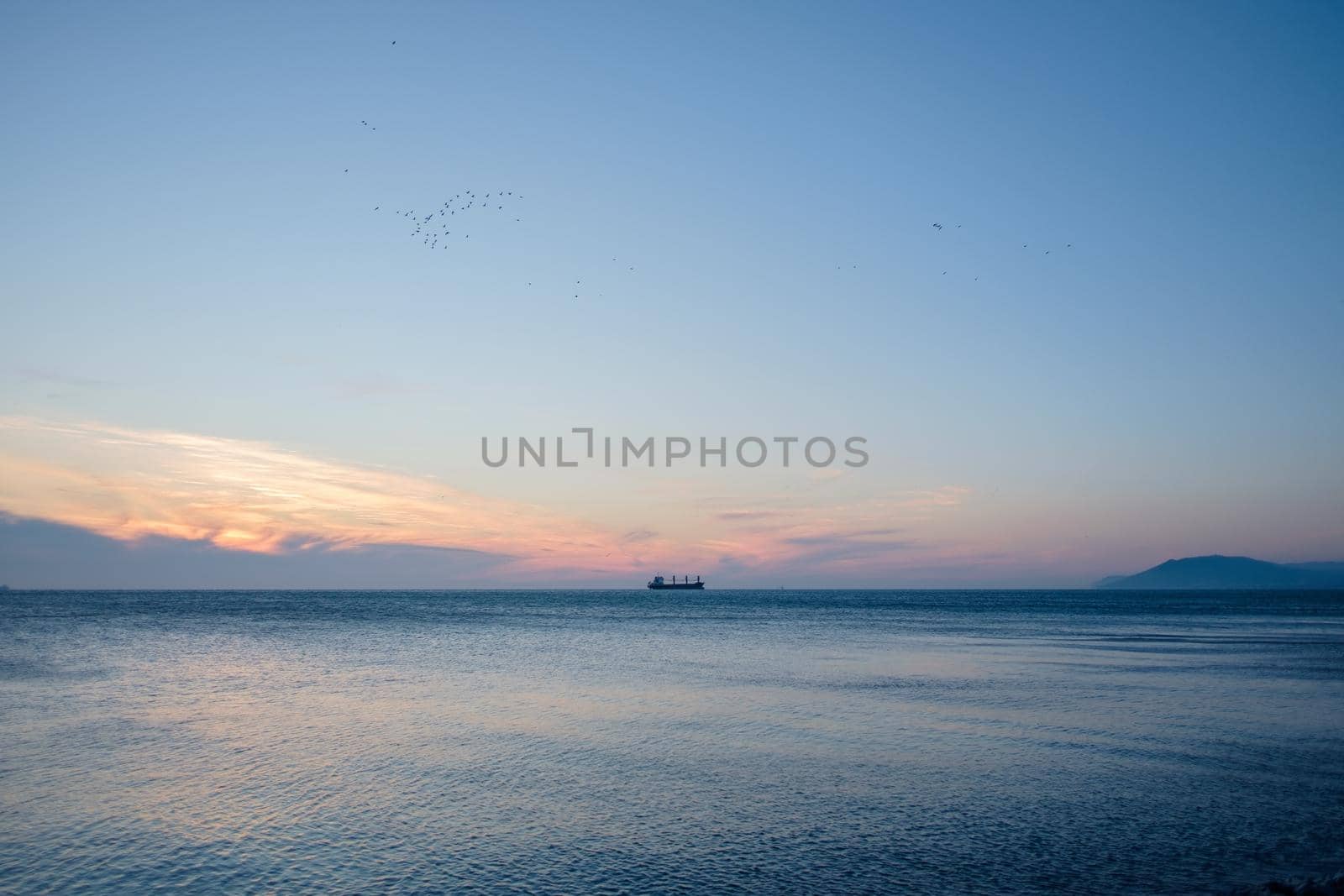 Ship sailing at horizon in the blue sea at sunset.