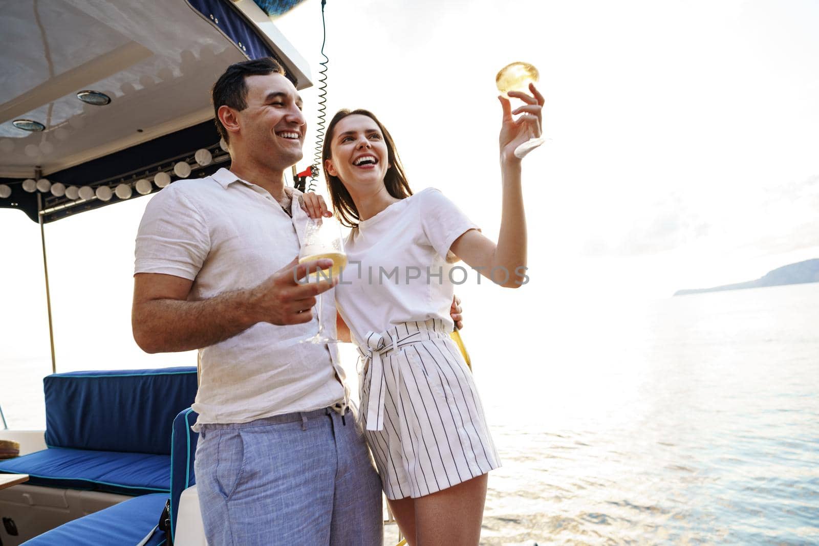 Young loving couple sitting on the yacht deck and drinking wine together