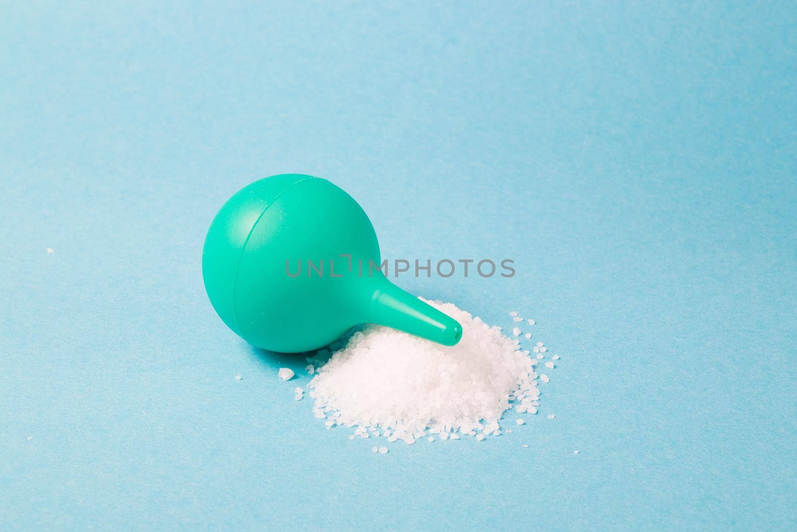 small green rubber enema with a handful of sea salt on a light blue background, copy space, rinsing the nose with salt water to treat a runny nose, treating the common cold concept