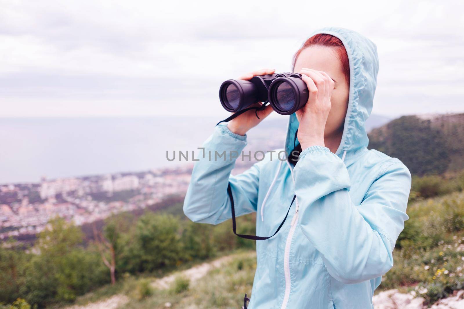 Traveler explorer young woman looking through binoculars in the mountains outdoor.