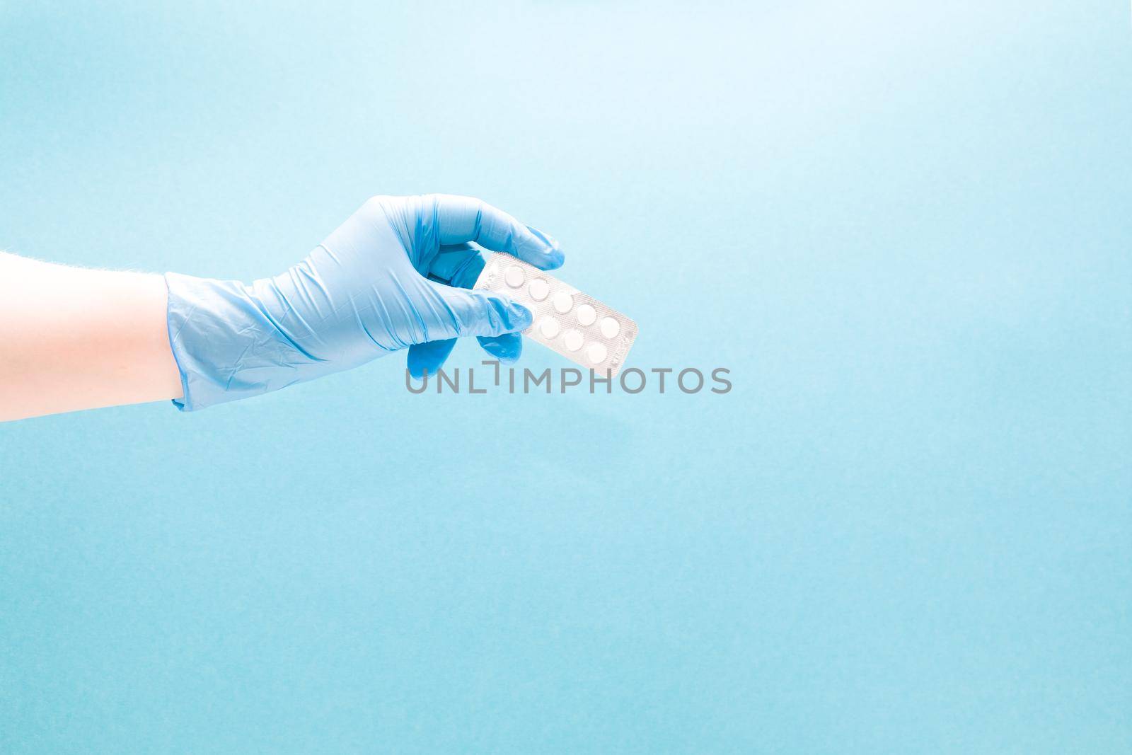 female hand in a blue disposable medical glove holds a blister with small white tablets on a blue background copy space