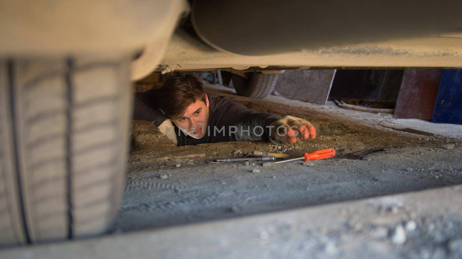 Man underneath a car reaching for a screwdriver for repairing car, close up