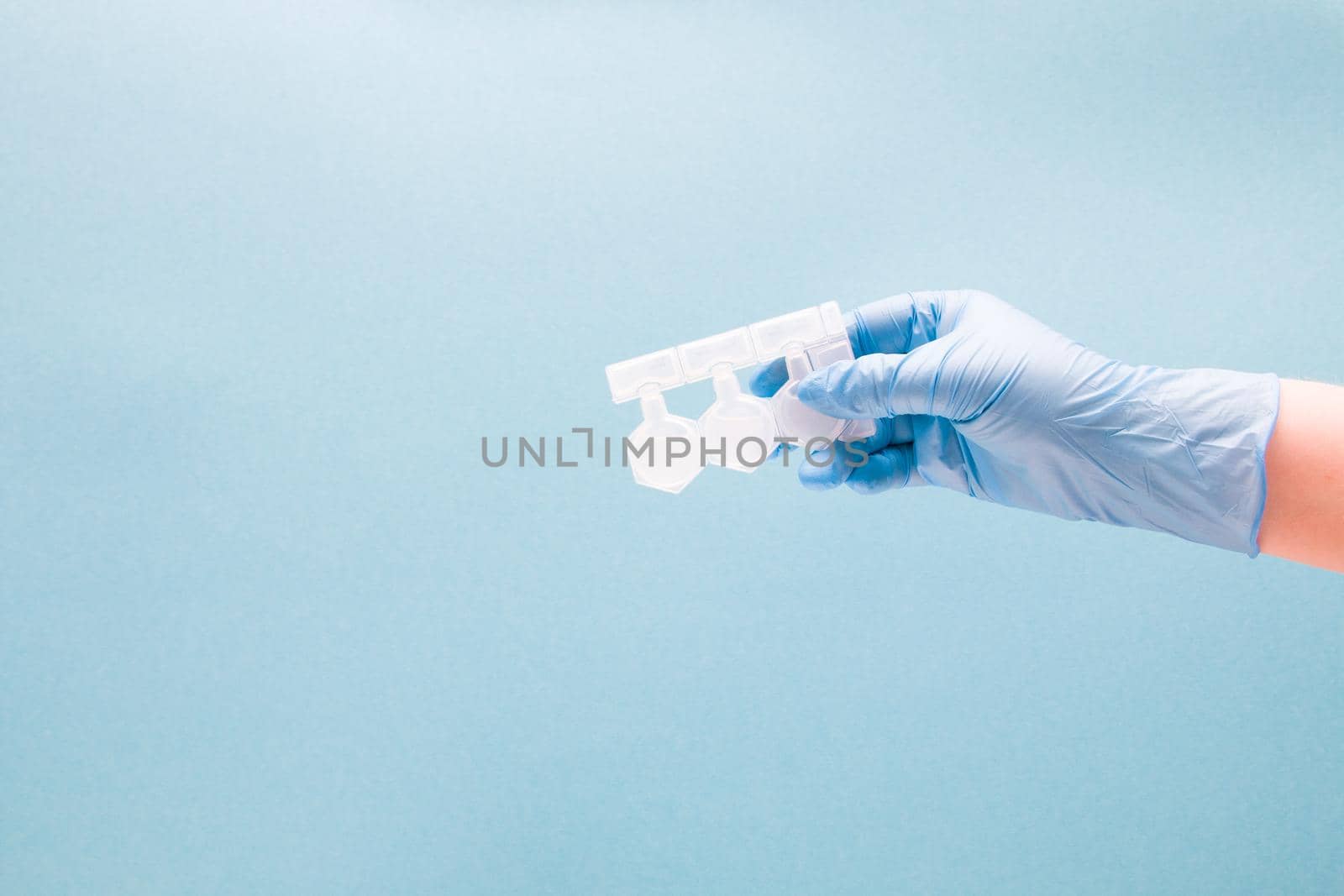 female hand in blue disposable medical glove holds containers with medication for inhalation, blue background copy space, treatment of asthma and bronchospasm, pulmonoligia concept