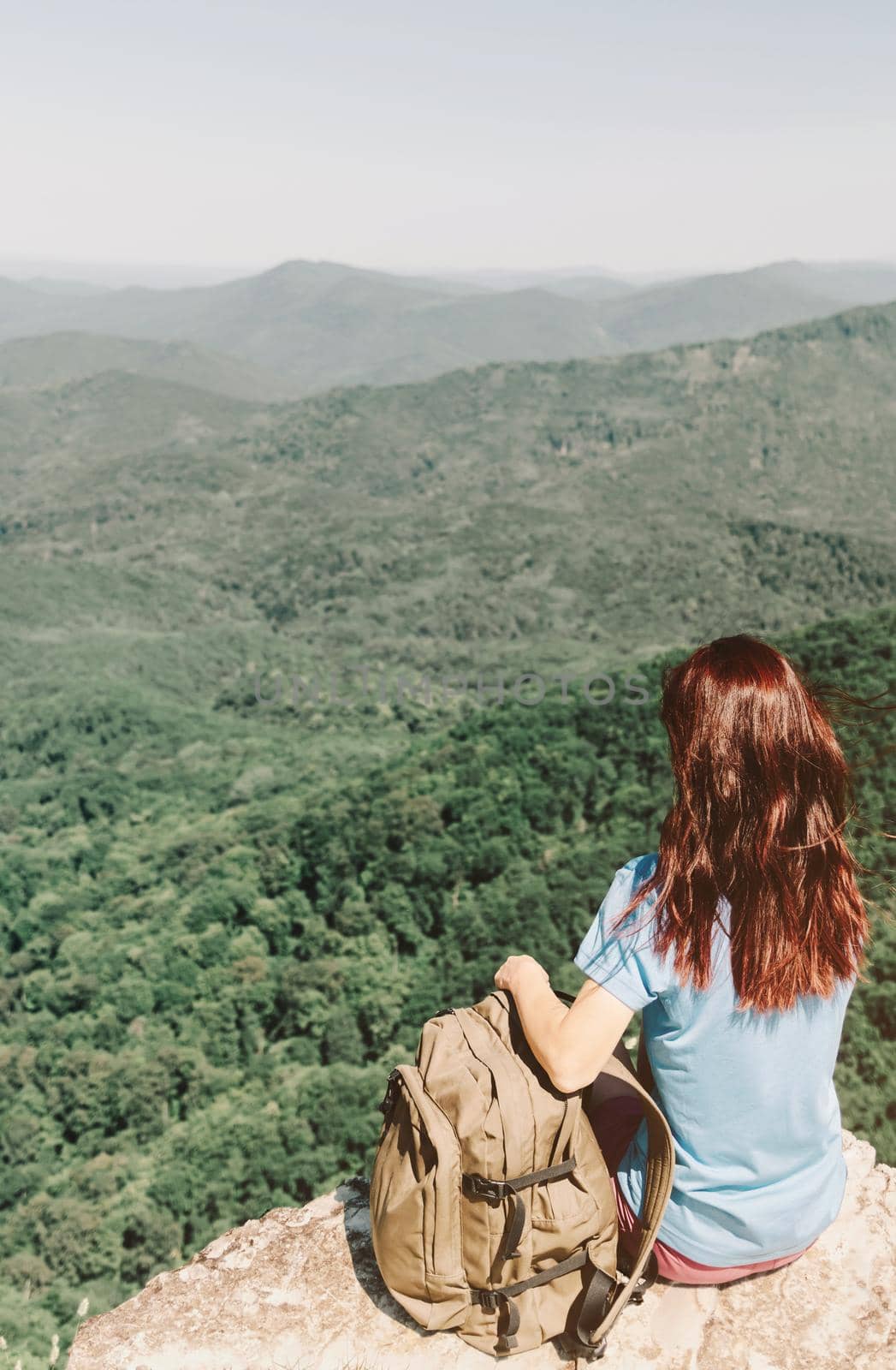 Woman with backpack resting on top of rock in front of summer mountains. by alexAleksei