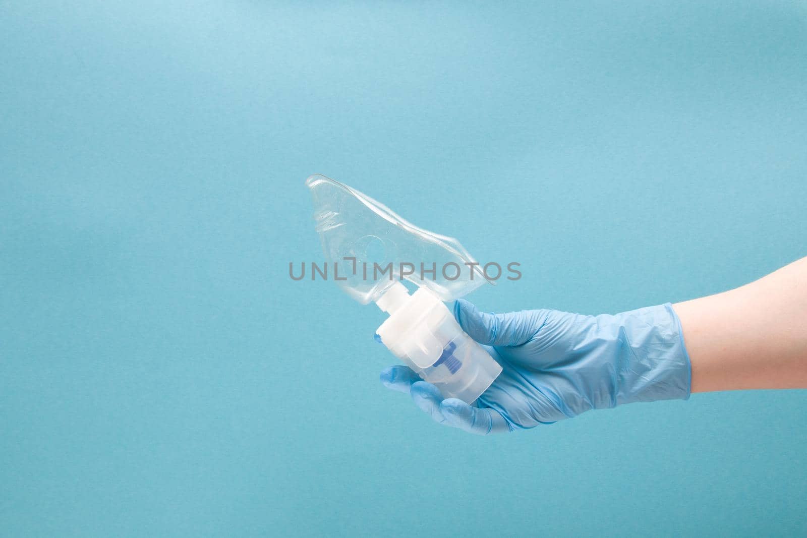 female hand in blue disposable medical glove holds nebulizer drug reservoir with silicone mask, inhalation device, pulmonology concept, blue background, copy space by natashko