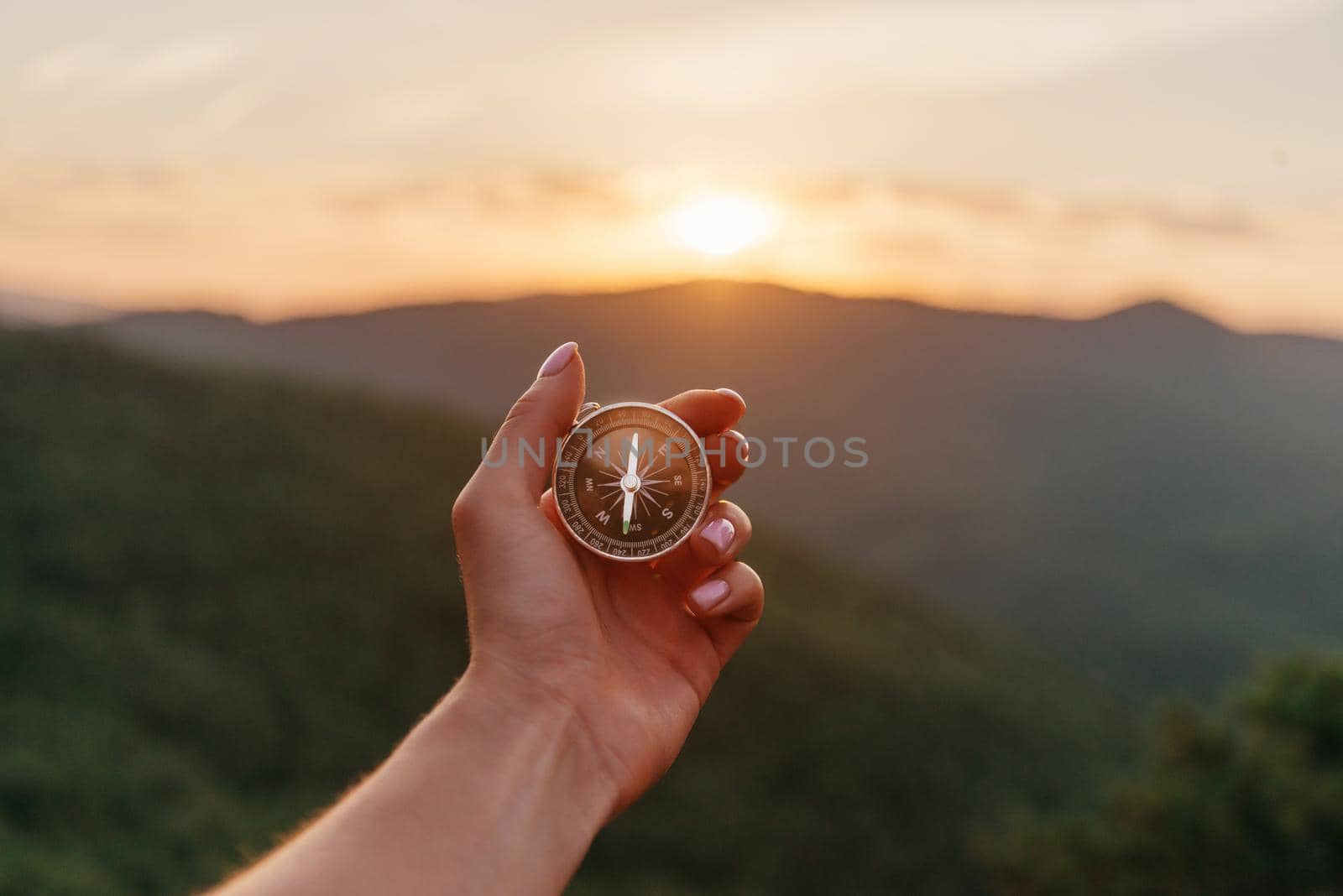 Explorer young woman holding compass in hand in summer mountains at sunrise, point of view. Concept of hiking and travel.