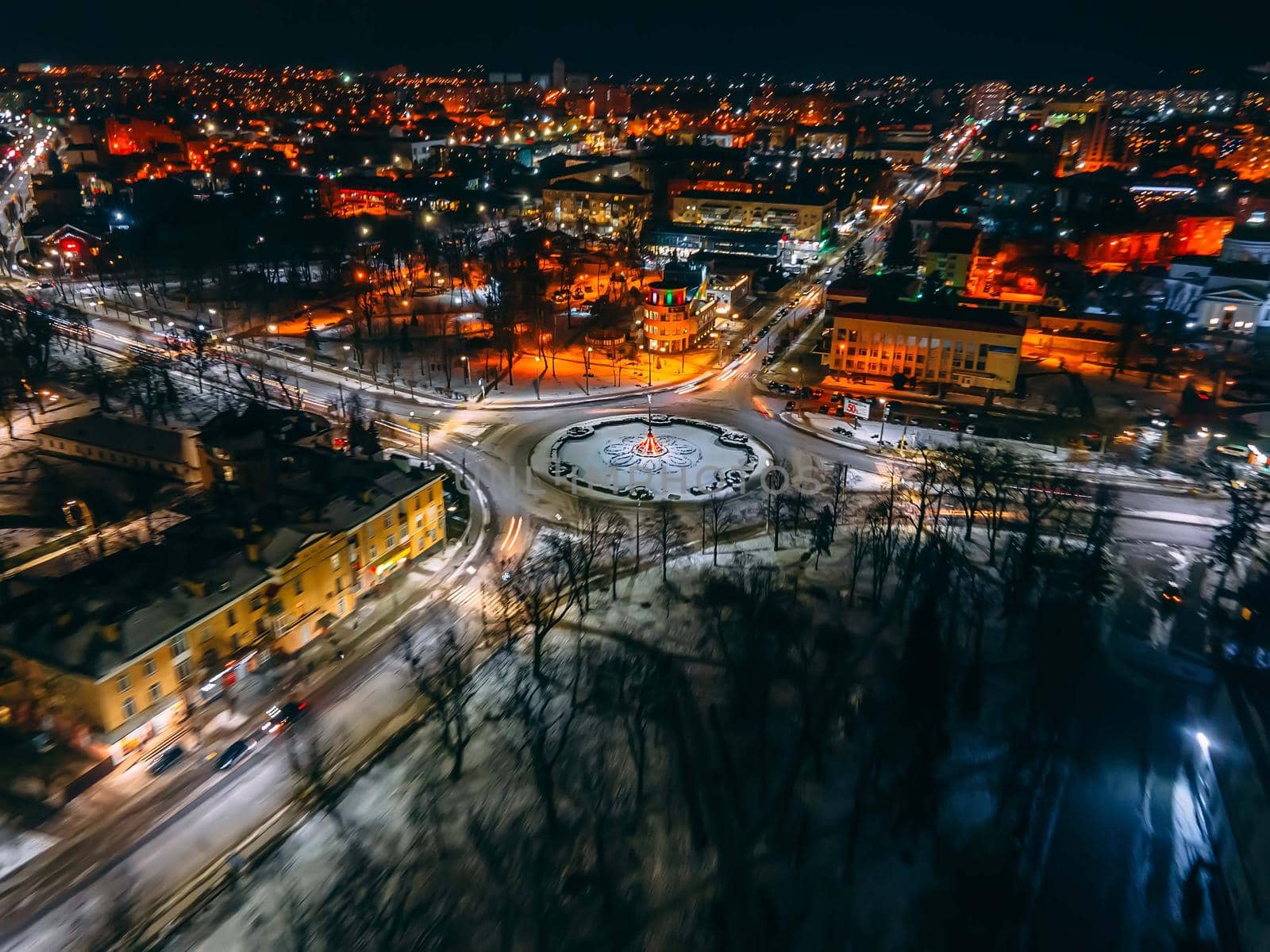 Aerial view of roundabout road with circular cars in small european city at winter night, long exposure. Kyiv region, Ukraine