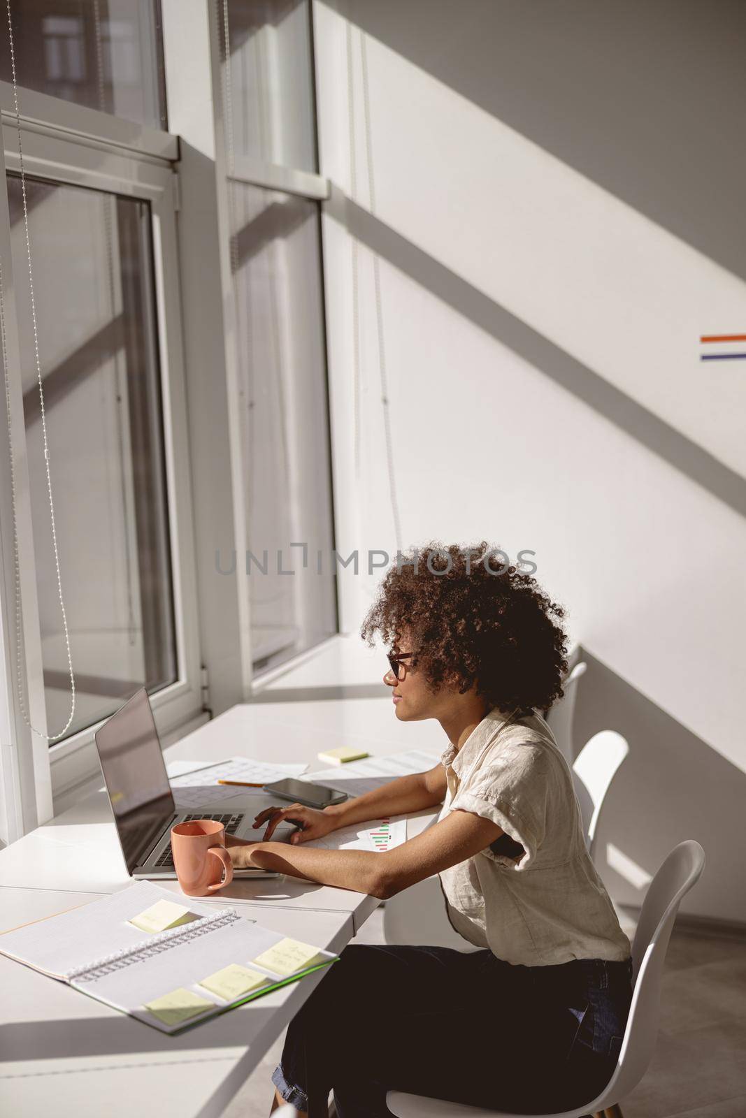 Side view of smiling young lady typing on laptop while working at the office