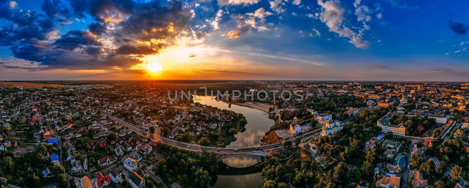 Aerial panorama view of small european city placed on river banks at summer sunny day with clouds by OnPhotoUa