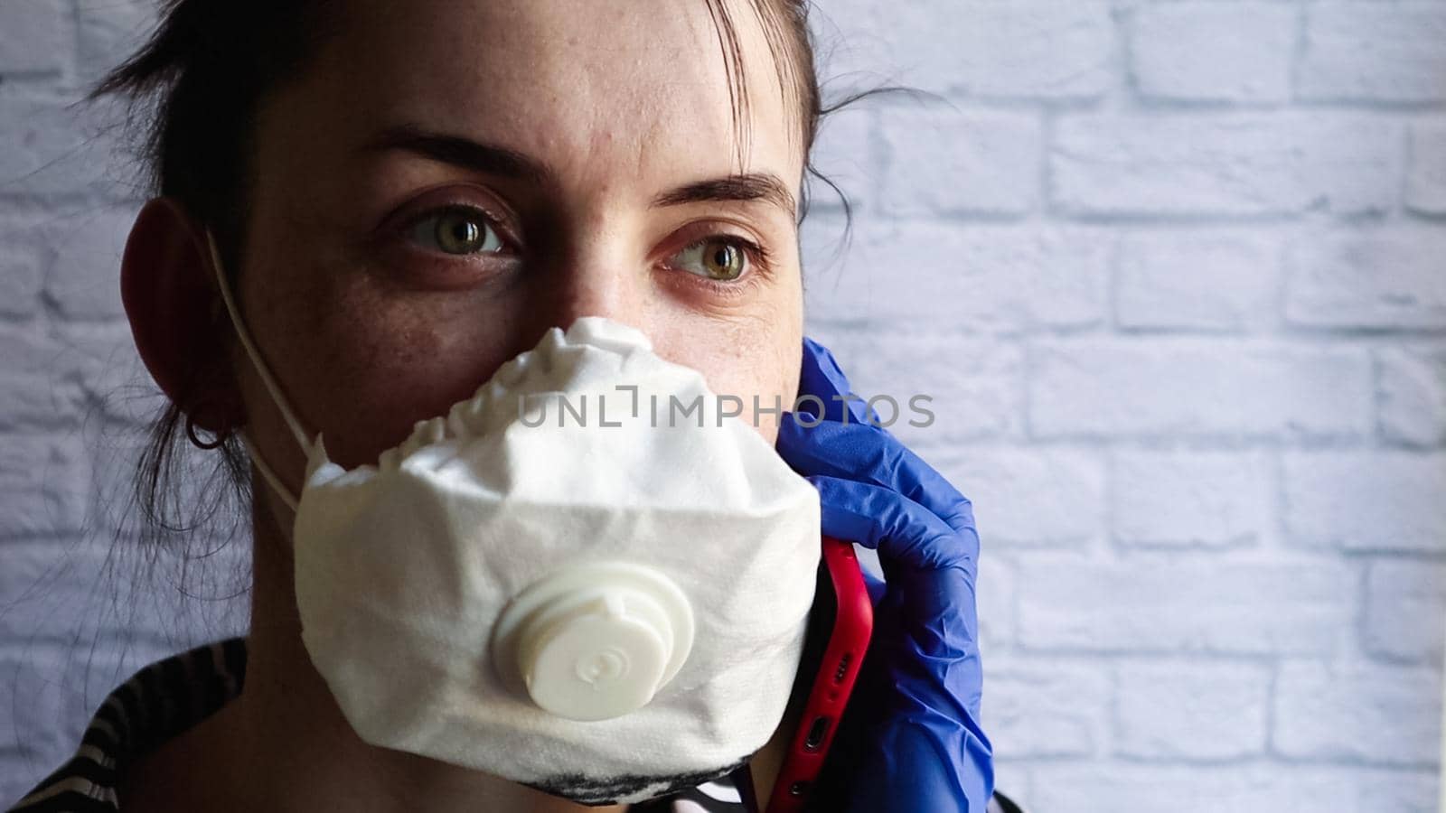 Young woman talking on the phone in a white mask. Coronavirus protection. epidemic precautions. A brunette in a medical mask holds a phone and talks on it. Quarantine in the world by Roshchyn
