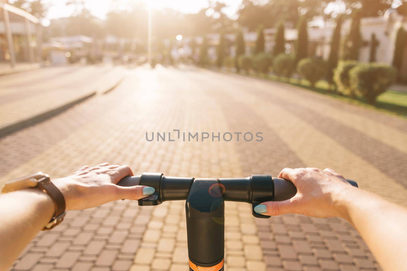 Unrecognizable young woman riding an electric scooter in city park in summer outdoor, point of view in first person.