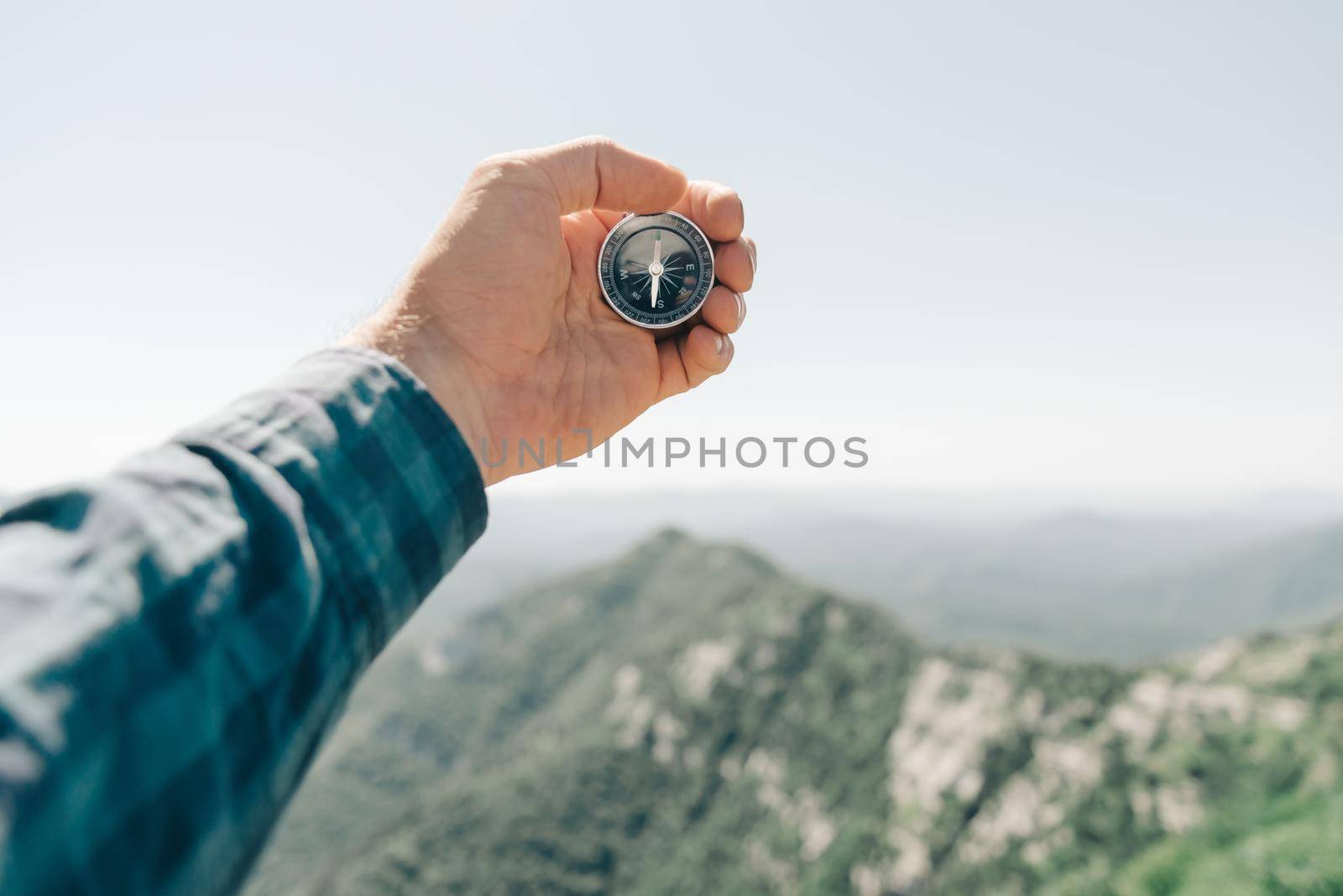 Man holding compass in hand in front of summer mountains, pov. by alexAleksei