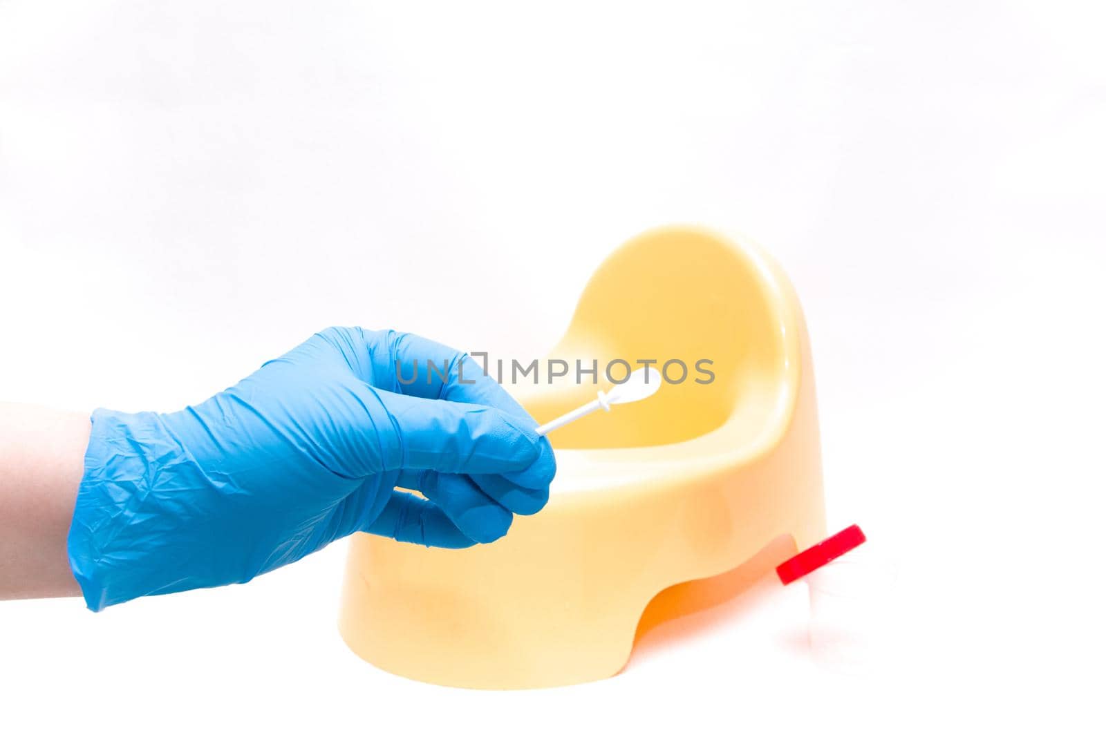 a hand in a disposable blue medical glove holds a white spatula for collecting feces, against the background is a yellow children's pot, white background, copy space
