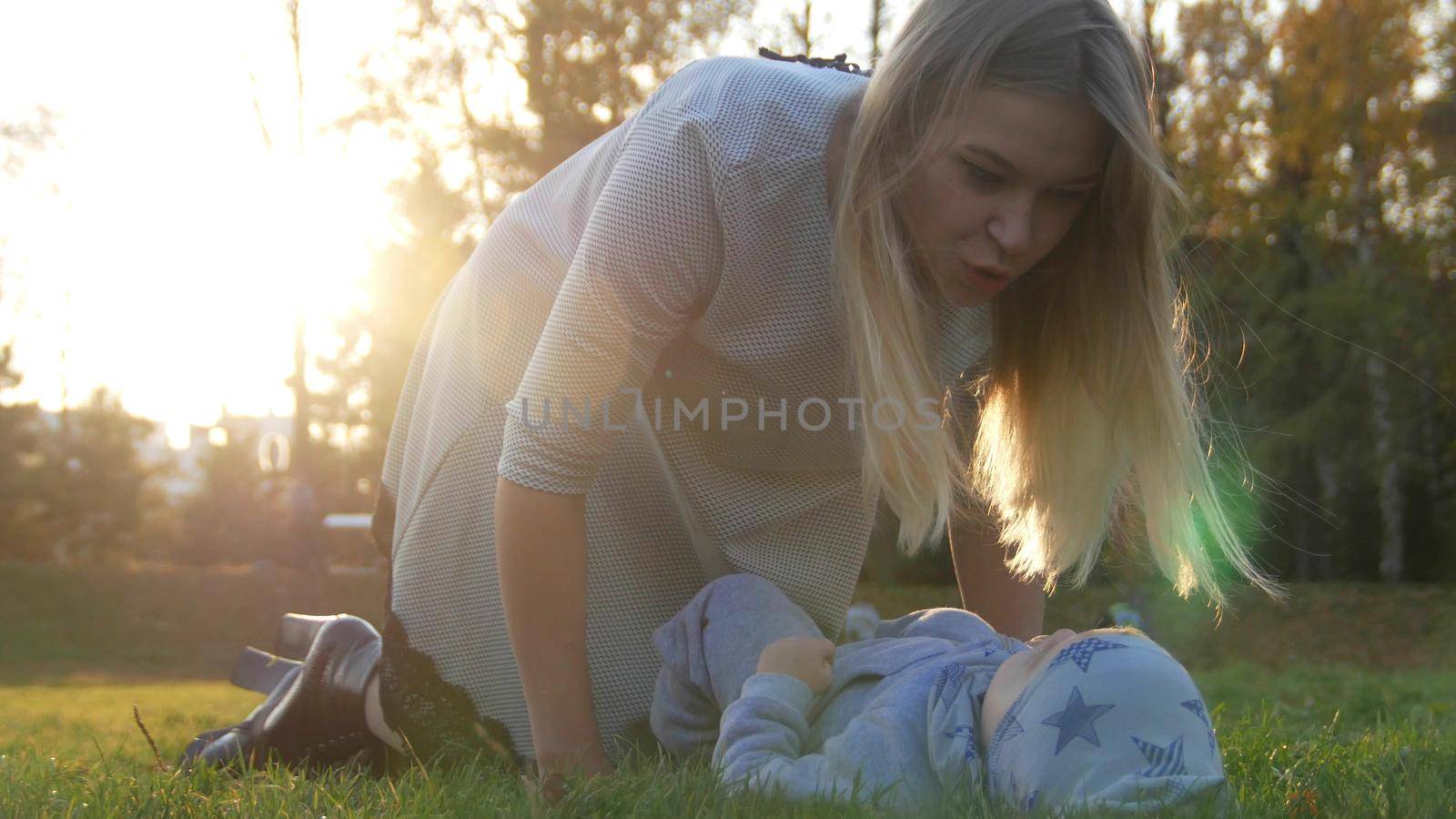 Young mother and her little baby playing in park. The baby lying on the grass. Close up. Wide shot
