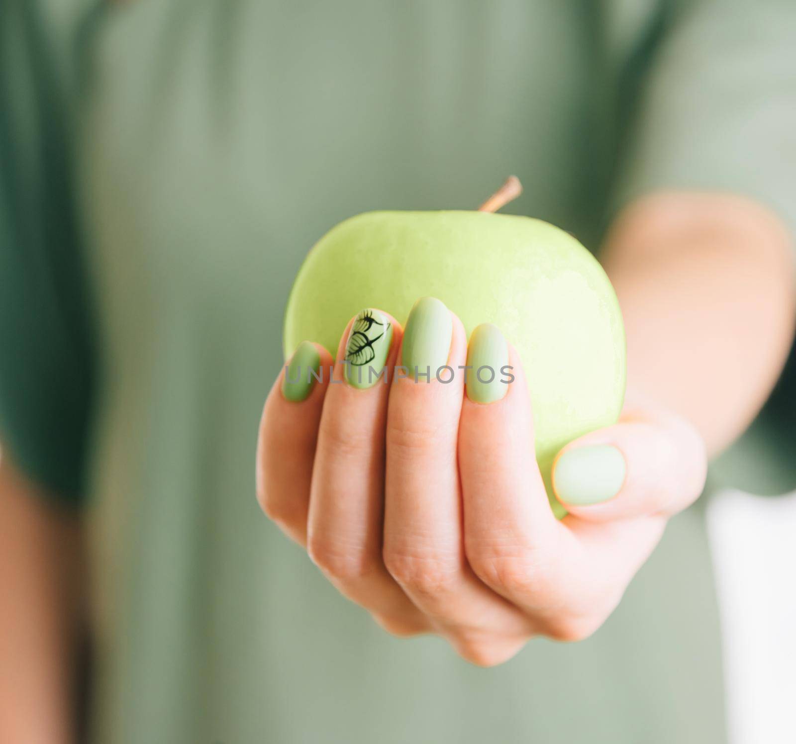 Female hand with beautiful green color manicure holding an apple.