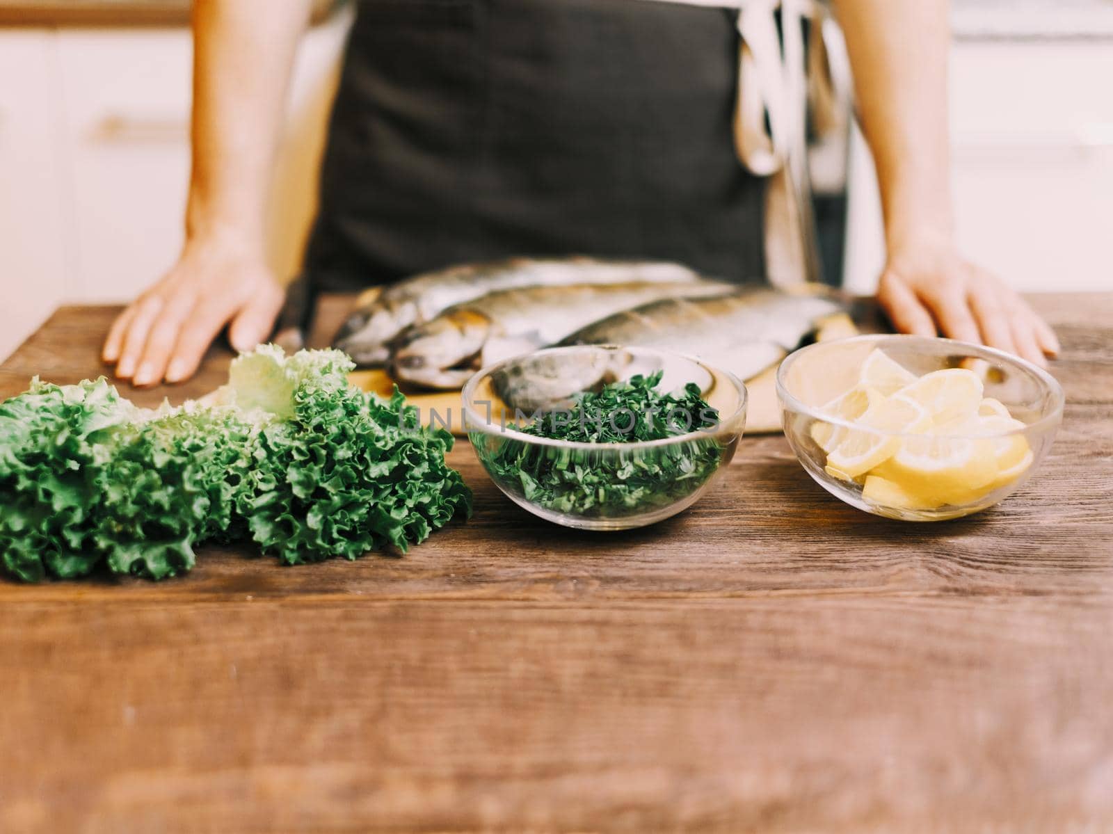 Unrecognizable woman cooking in the kitchen, food ingredients for fish dish on wooden table.