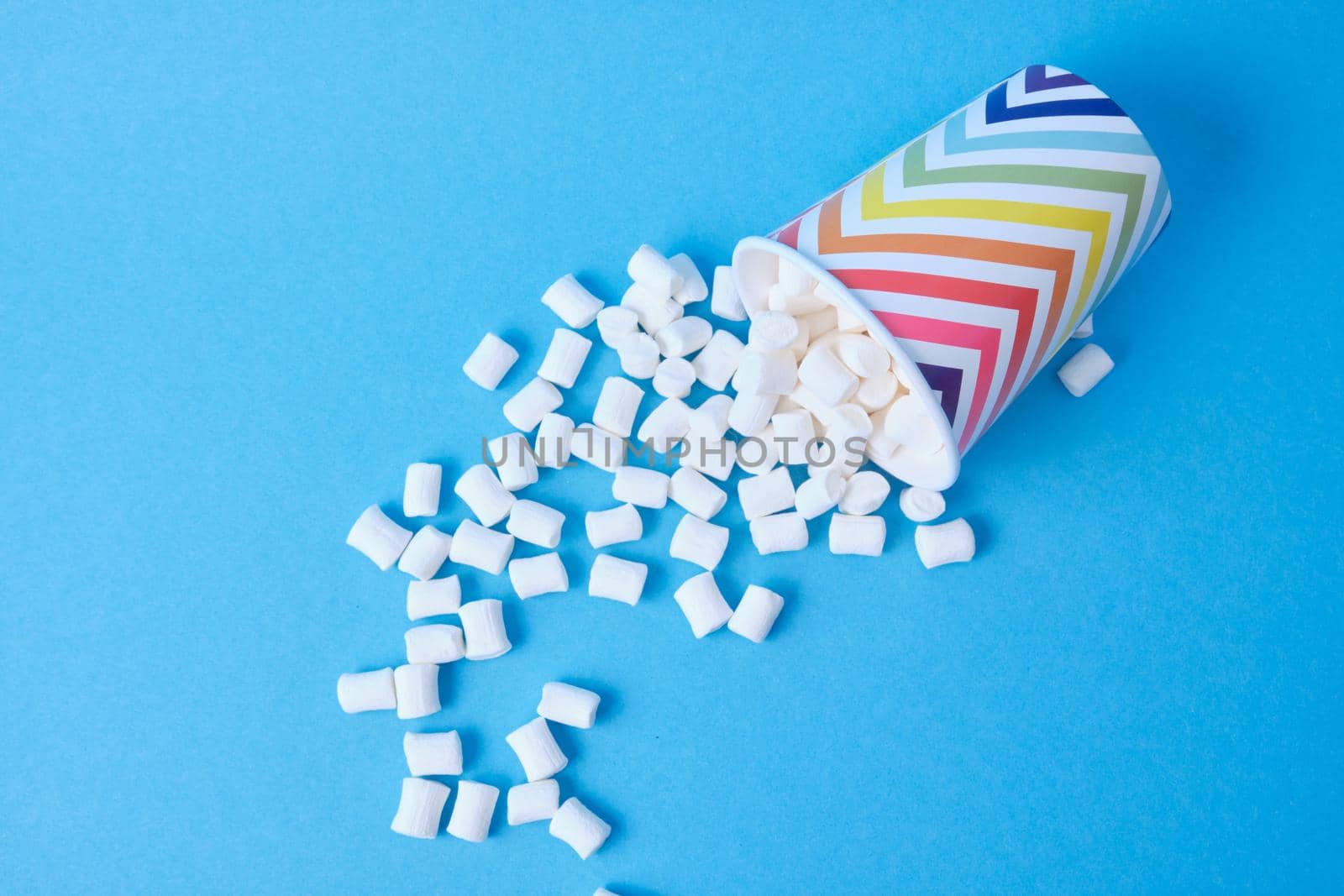 marshmallows dropped out of their holiday paper cups with geometric pattern on blue background, copy space