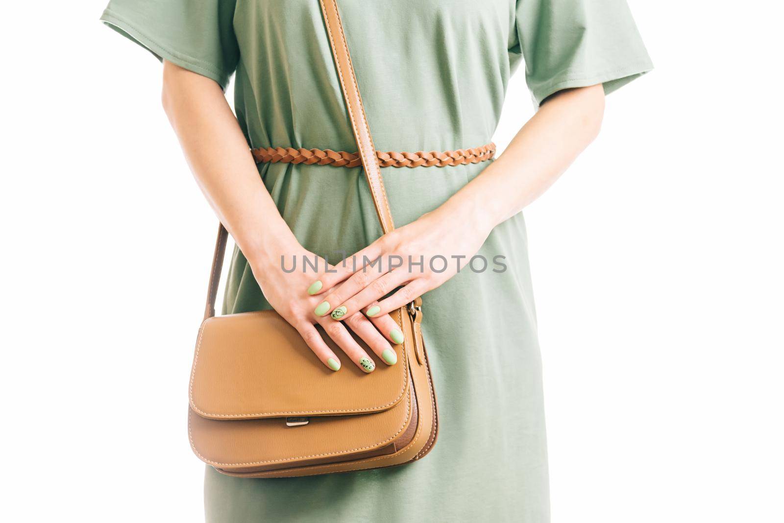 Unrecognizable young woman in green dress standing with brown handbag. Casual style, female beauty and fashion. Studio shot.