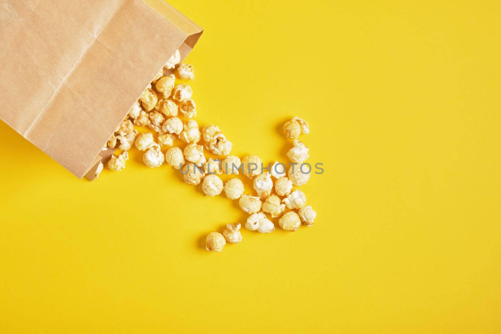 Caramel popcorn in a paper bag on yellow background.copy space top view