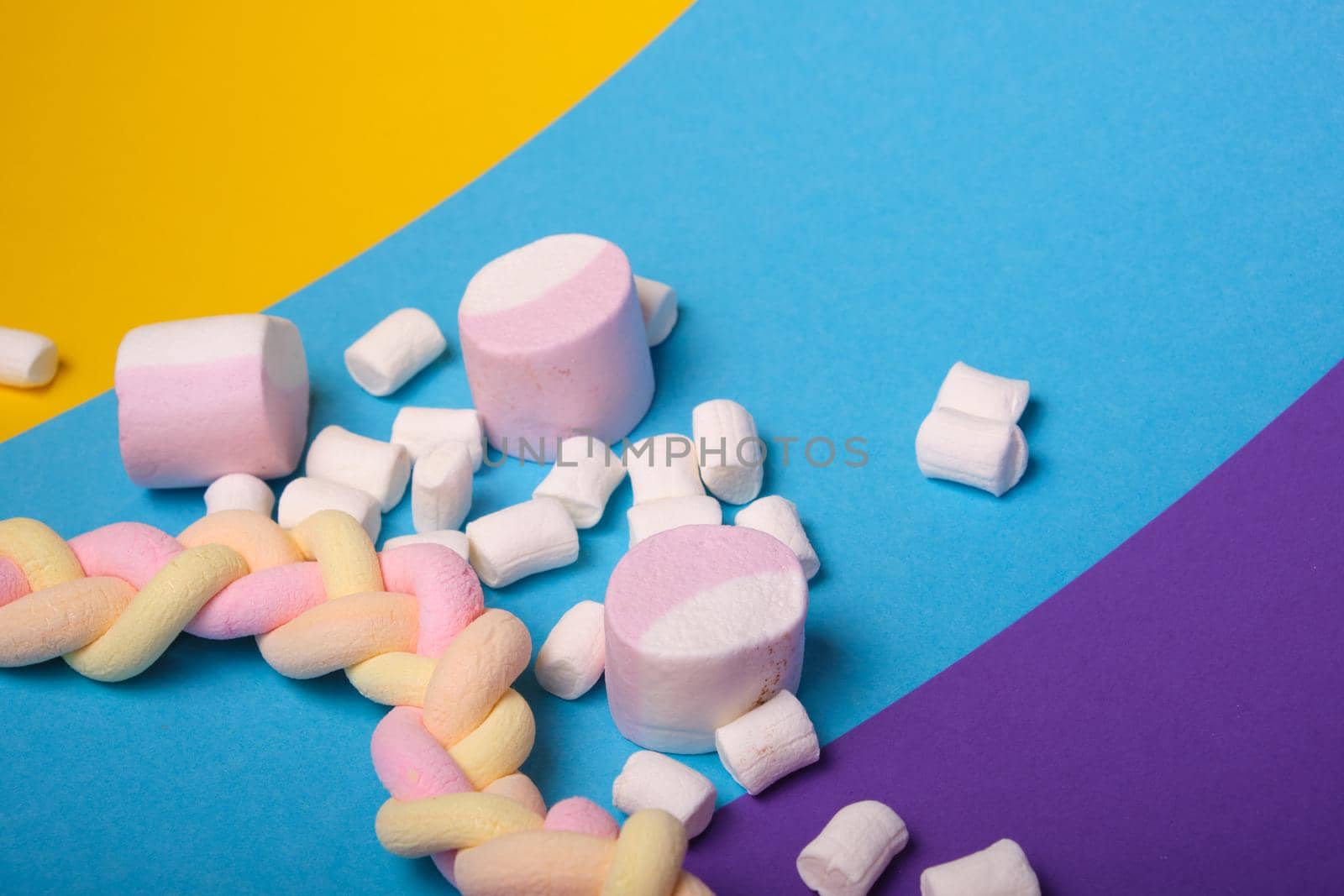 different types of marshmallows with different flavors on a bright colored background, long spaghetti-shaped marshmallows are braided in a pigtail
