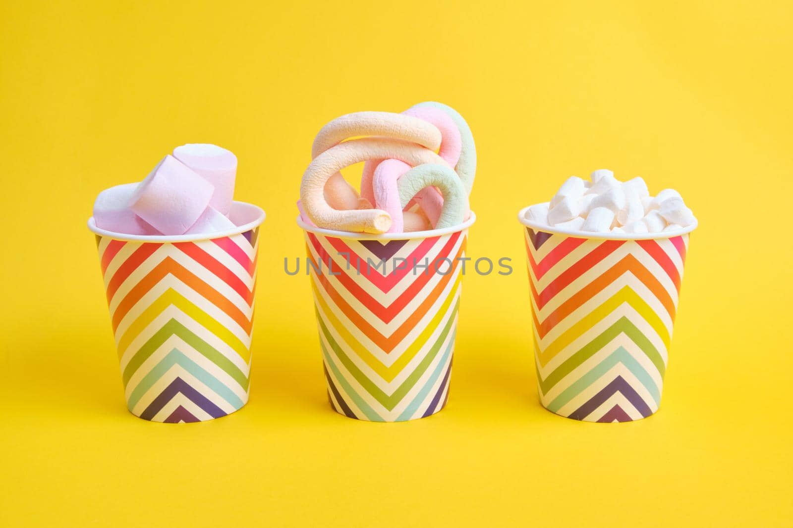 different types of marshmallows in festive paper cups with geometric pattern on yellow background, copy space by natashko