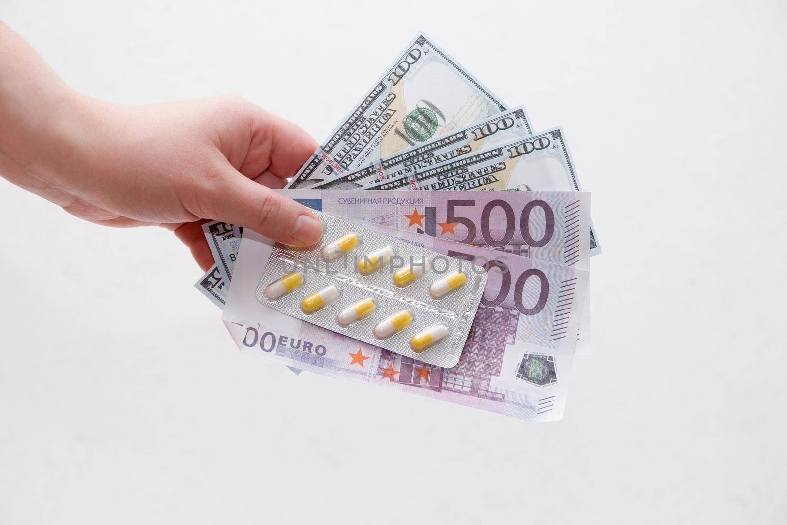 female hand holds a pack of yellow capsule pills and dollar bills euro and dollars, white background