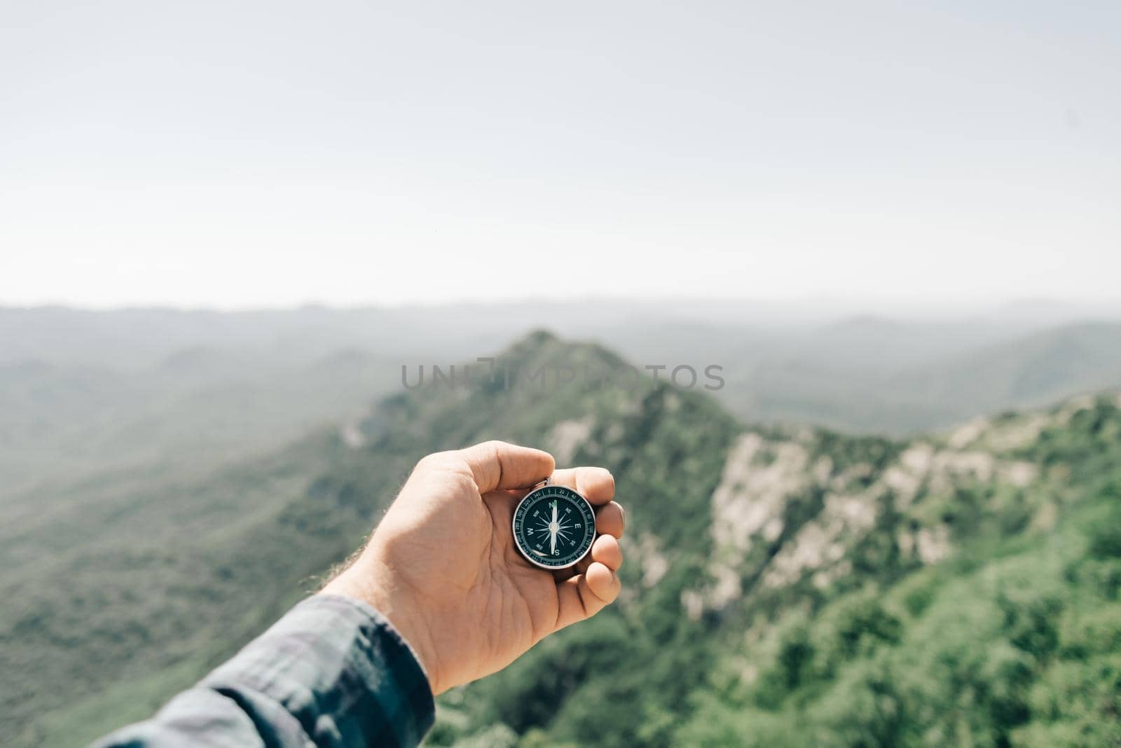 Male hand with magnetic compass high in summer mountains, point of view. Concept of travel and hiking.